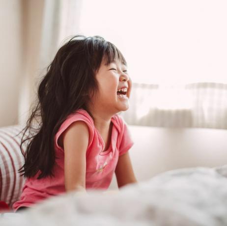 Maza meitene priecīgi smejas gultā