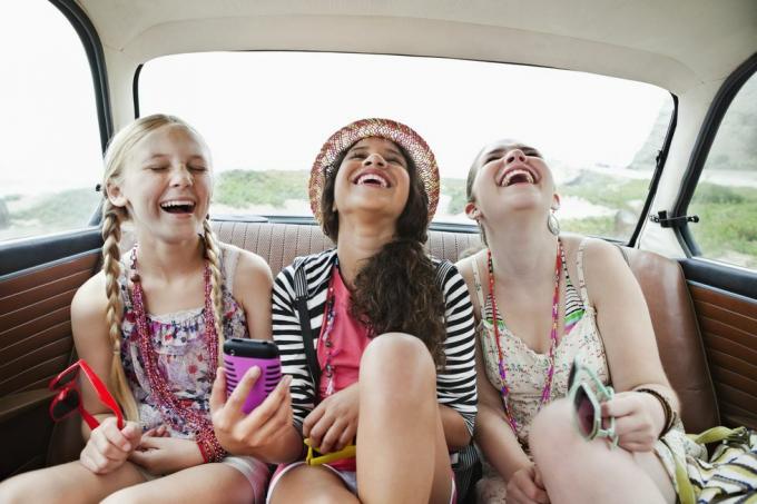 trīs meitenes smejas automašīnas aizmugurējā sēdeklī