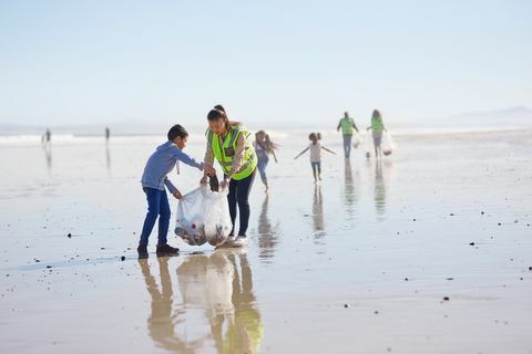 Māte un dēls brīvprātīgie tīra pakaišus saulainā, mitrā smilšu pludmalē