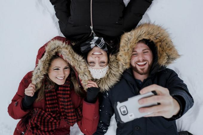 Draugi no augsta leņķa uzņem selfiju, guļot uz sniega klāta lauka