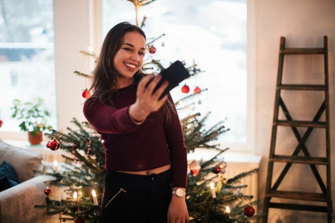 sieviete, kas uzņem selfiju Ziemassvētku eglītes priekšā