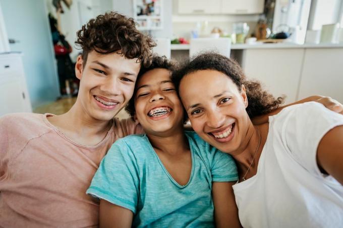 portrets, kurā redzama vientuļā mamma, kas sēž uz dīvāna ar diviem dēliem mājās