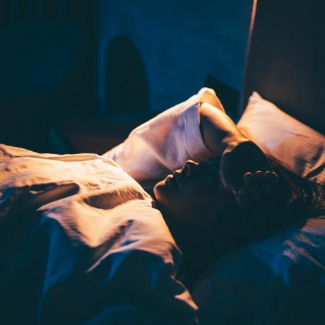sieviete ar bezmiegu jauna sieviete guļ gultā ar roku uz pieres