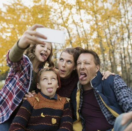 Muļķīga ģimene, kas uzņem selfijus, veido sejas rudens parkā