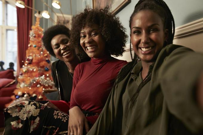 trīs jaunas sievietes taisa selfiju dīvānā pie Ziemassvētku eglītes mājās
