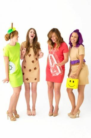 četras smejošās sievietes īsās kleitās, tērpušās kā "pusdienu dāmas", viena nēsāja pusdienu kastīti ar dzeltenu smaidiņu